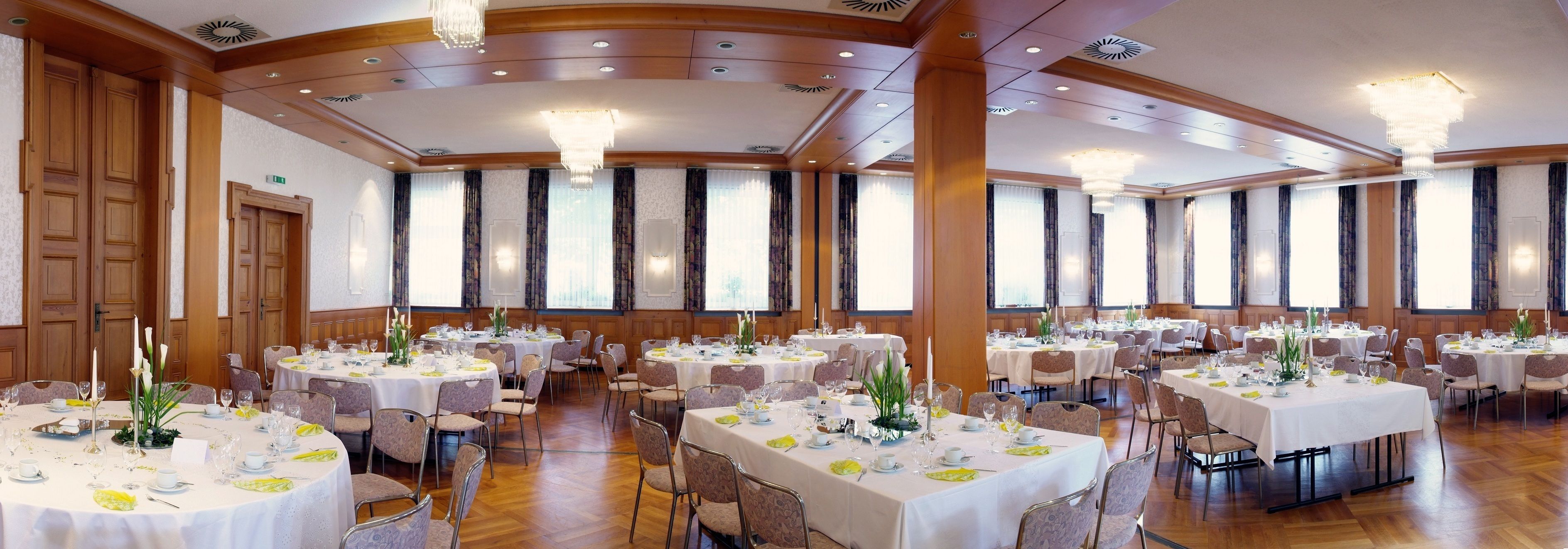 Un salón de banquetes con varias mesas redondas dispuestas para cenar, con manteles blancos, centros de mesa florales y candelabros.