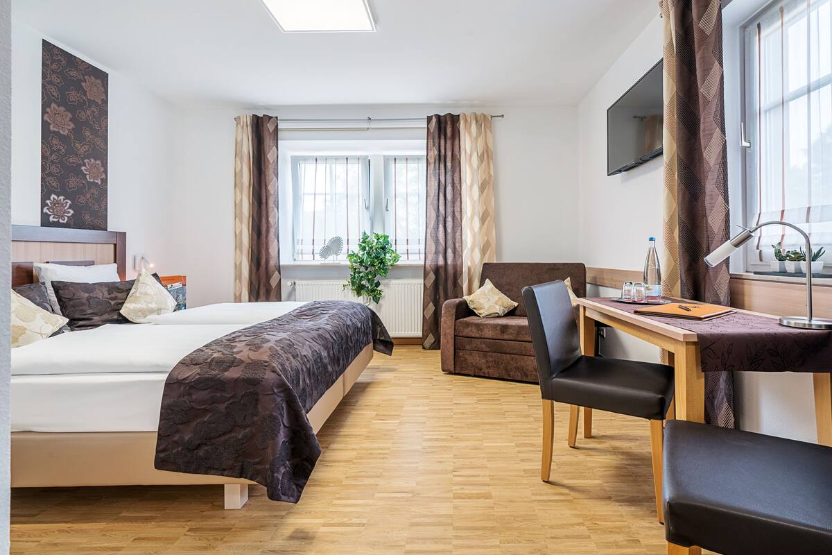 Ein Hotelzimmer mit Bett, Schreibtisch, Stuhl, Fernseher und einem Fenster mit Vorhängen.