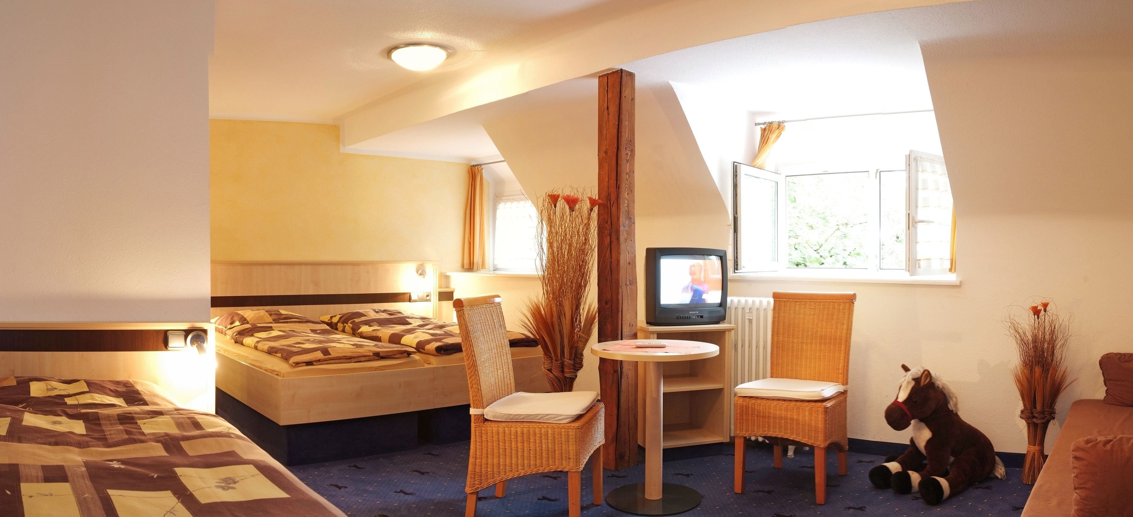 A hotel room with a bed, two chairs, a small table, a television, and a window with curtains.