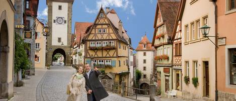 A cobblestone street lined with traditional half-timbered buildings, a clock tower, and a bench.