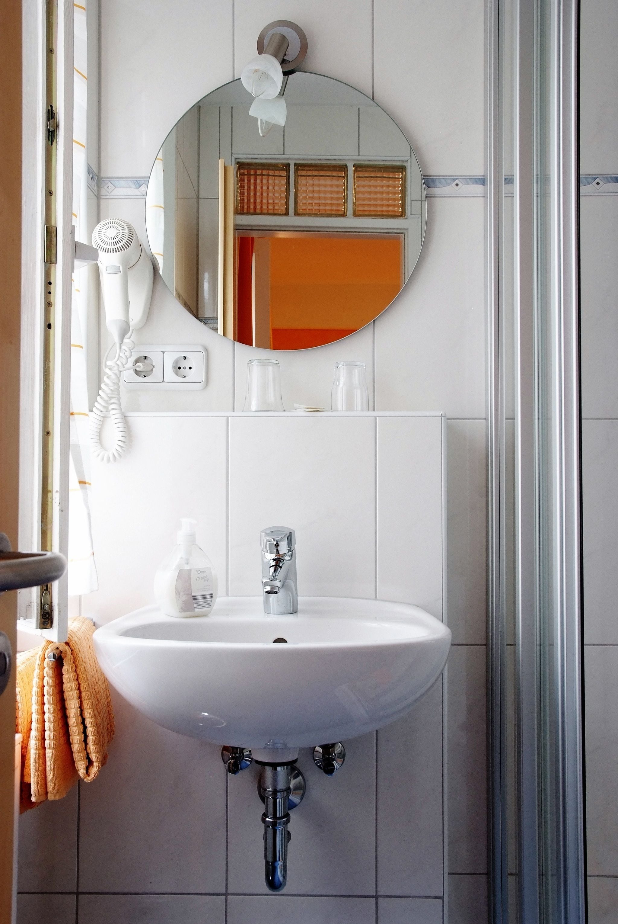 Un baño con lavamanos blanco, espejo, secador de pelo y toallero.