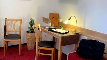 A hotel room with a desk, two chairs, a bed, a TV, and a red carpet with animal prints.