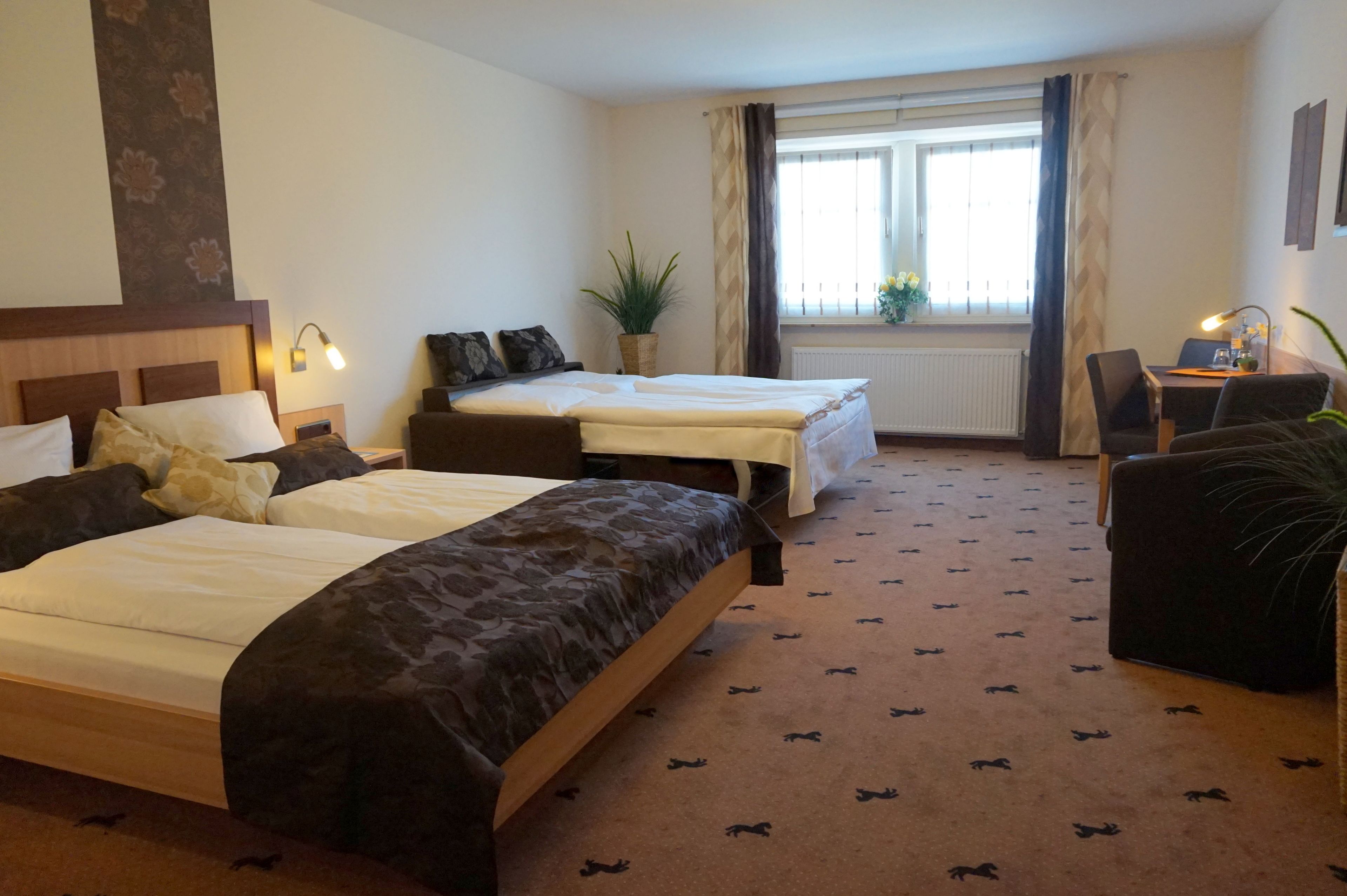 Habitación de hotel con dos camas, un escritorio, una silla, una planta en maceta y una ventana con cortinas.