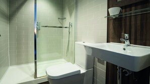 A modern bathroom with a glass shower enclosure, a white toilet, and a white sink with a cup holder.