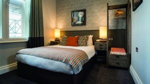 A hotel room with a large bed, two bedside tables with lamps, a nightstand, a wardrobe, and a wall clock.