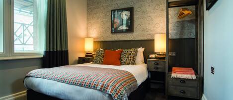 A hotel room with a large bed, two bedside tables with lamps, a nightstand, a wardrobe, and a wall clock.
