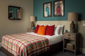 A neatly made bed with a plaid blanket, two bedside tables with lamps, and framed artwork on the wall. - Toll House Inn (Lancaster)