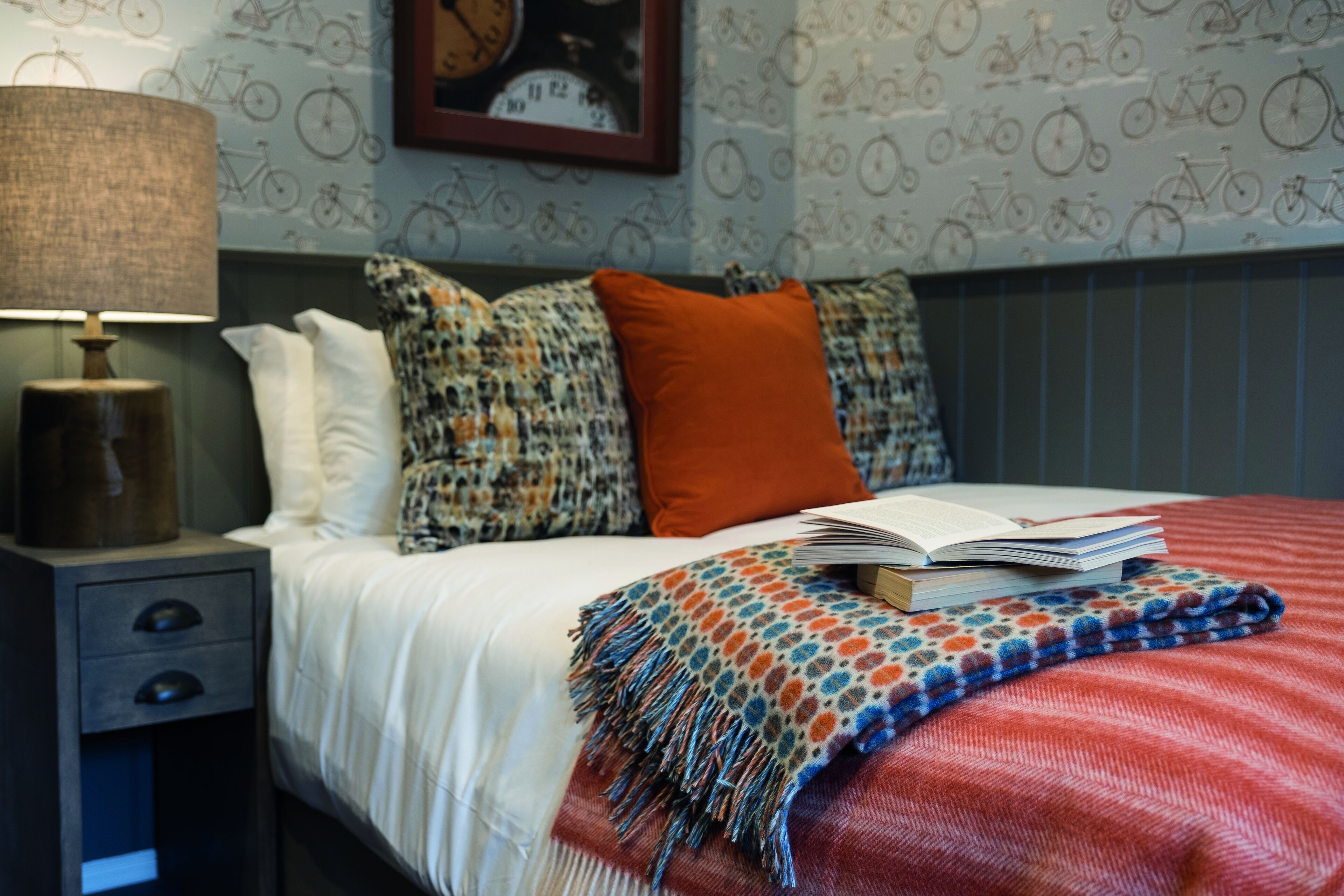 Un letto rifatto con una coperta a righe rosse e bianche, un libro e una coperta decorata.