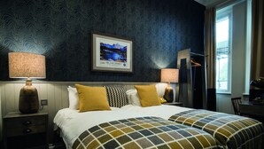 A hotel room with a large bed, two bedside lamps, a framed picture on the wall, and a window with curtains.