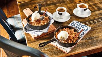 Una mesa de madera rústica con dos sartenes de hierro fundido que contienen postres y tazas de café.