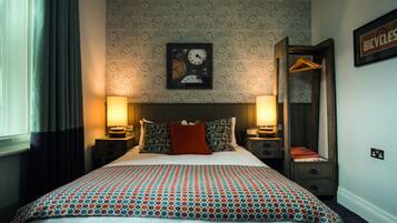 A neatly made bed with patterned bedding, two bedside lamps, a framed picture on the wall, and a bicycle-themed wallpaper.