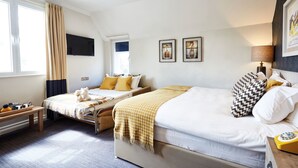 A hotel room with two beds, a flat-screen TV, artwork on the walls, and a window with curtains.