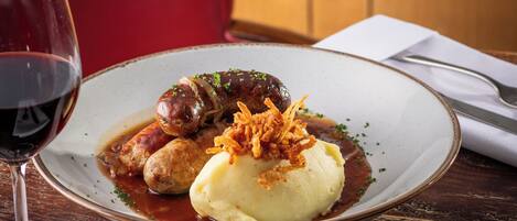 A plate of food with sausages, mashed potatoes, and a glass of red wine on a wooden table.