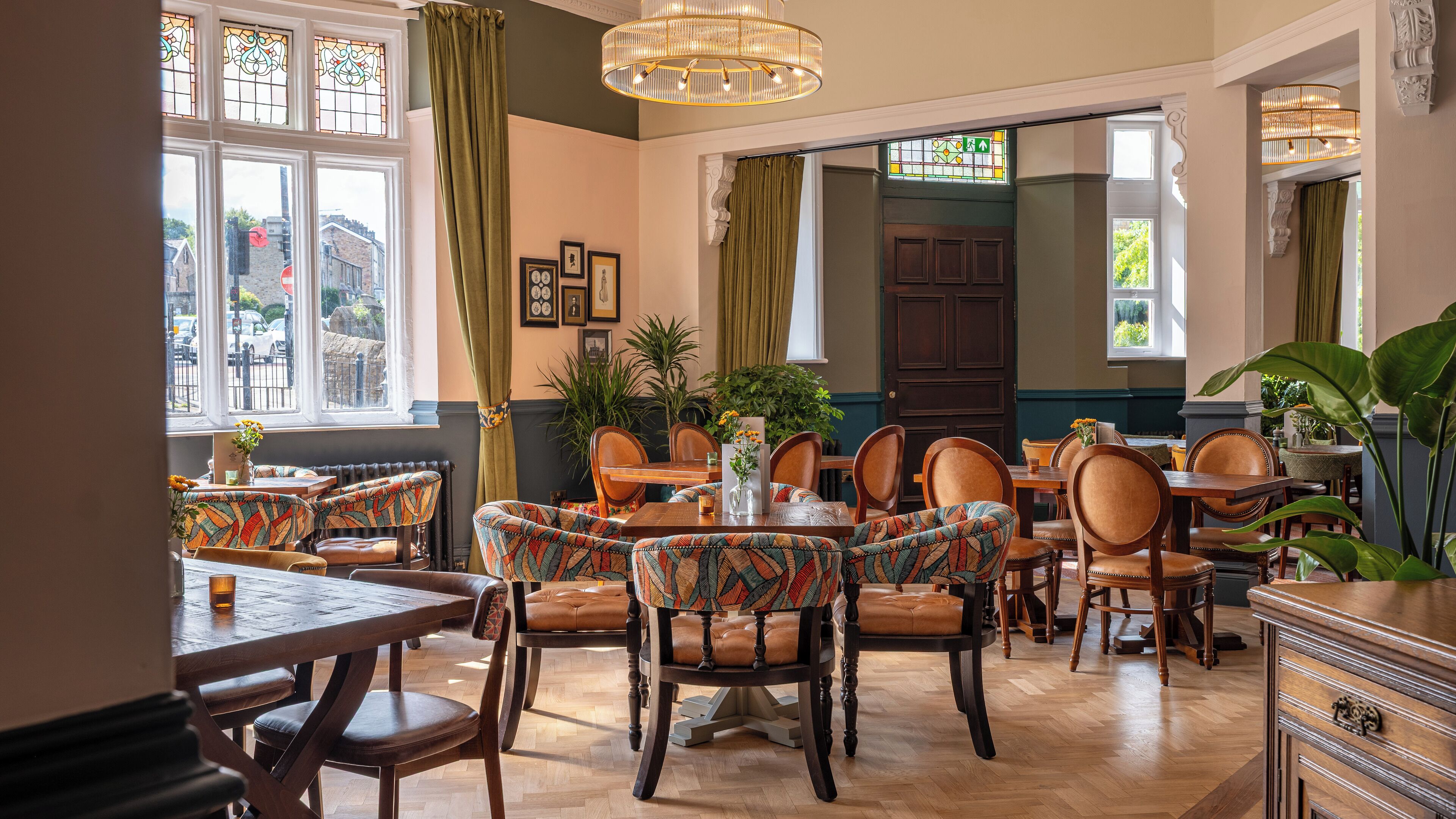 Un espace repas avec des tables et des chaises en bois, de grandes fenêtres avec des rideaux et un lustre.