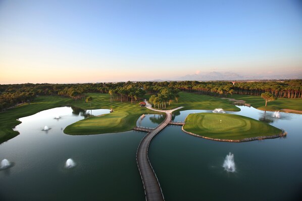 Un parcours de golf avec des obstacles d’eau, un pont et un club-house.