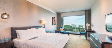 A modern hotel room with a large bed, a desk, a chair, and a view of the city.
