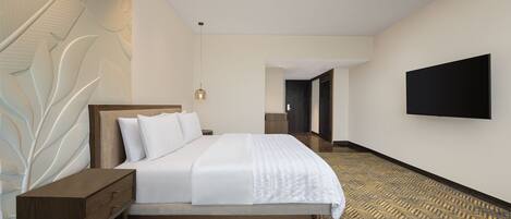 A modern hotel room with a large bed, a nightstand, a wall-mounted TV, and a patterned carpet.