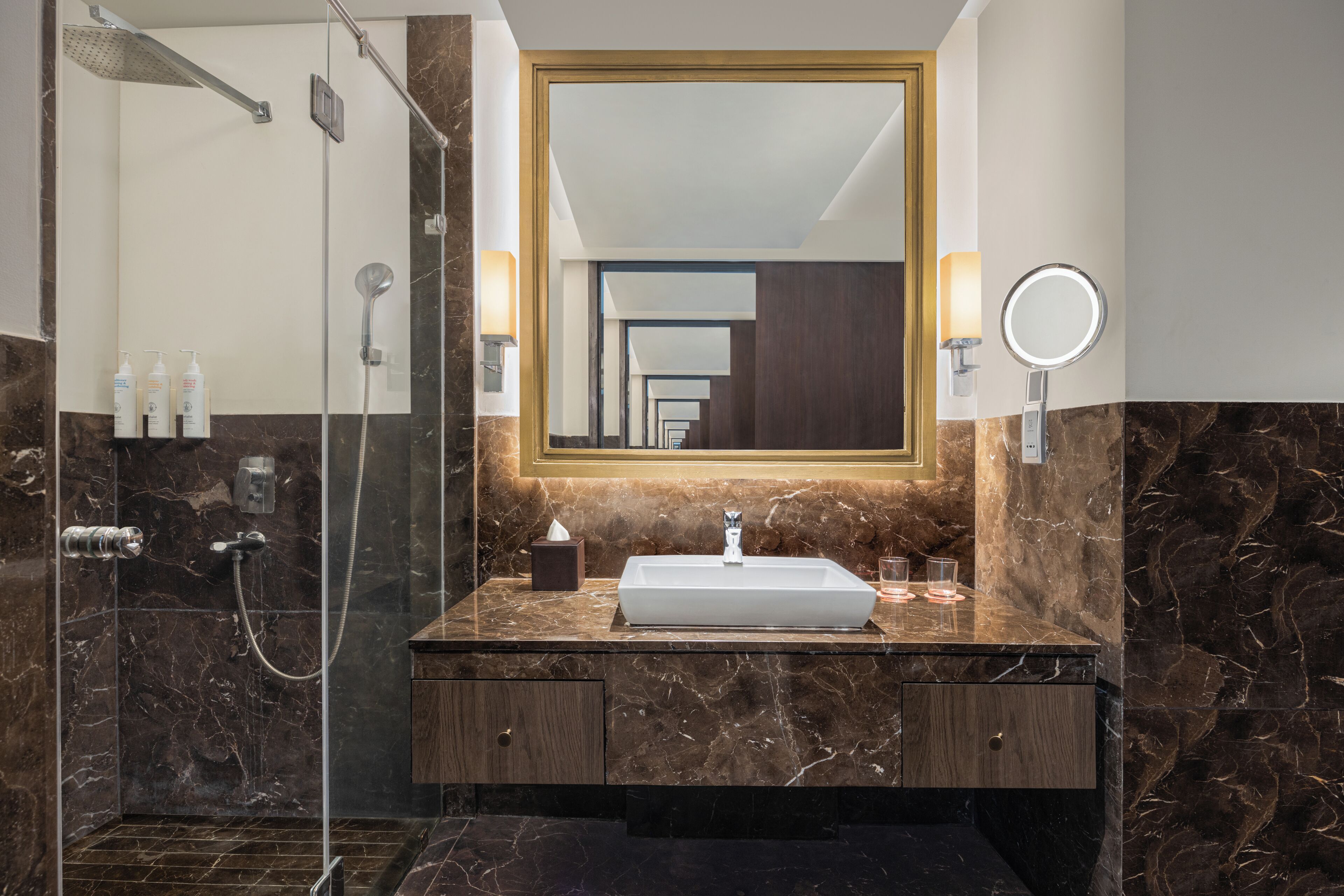 Une salle de bain dotée d’une douche à parois de verre, d’un meuble-lavabo en marbre et d’un grand miroir.