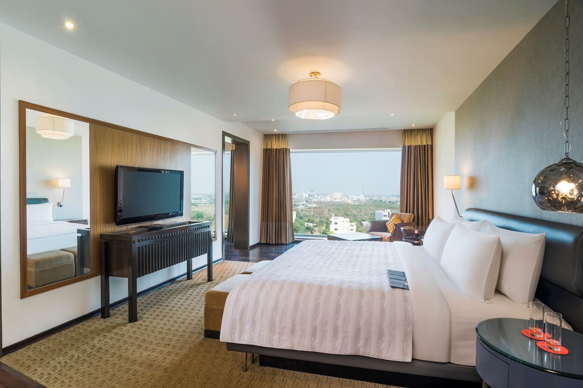 A hotel room with a bed, a television, a desk, and a view of the city.