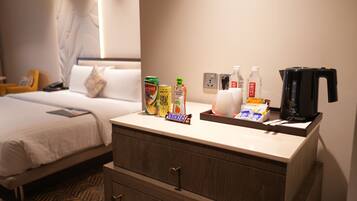 A hotel room with a bed, a bedside table with snacks, a coffee maker, and a wall socket.