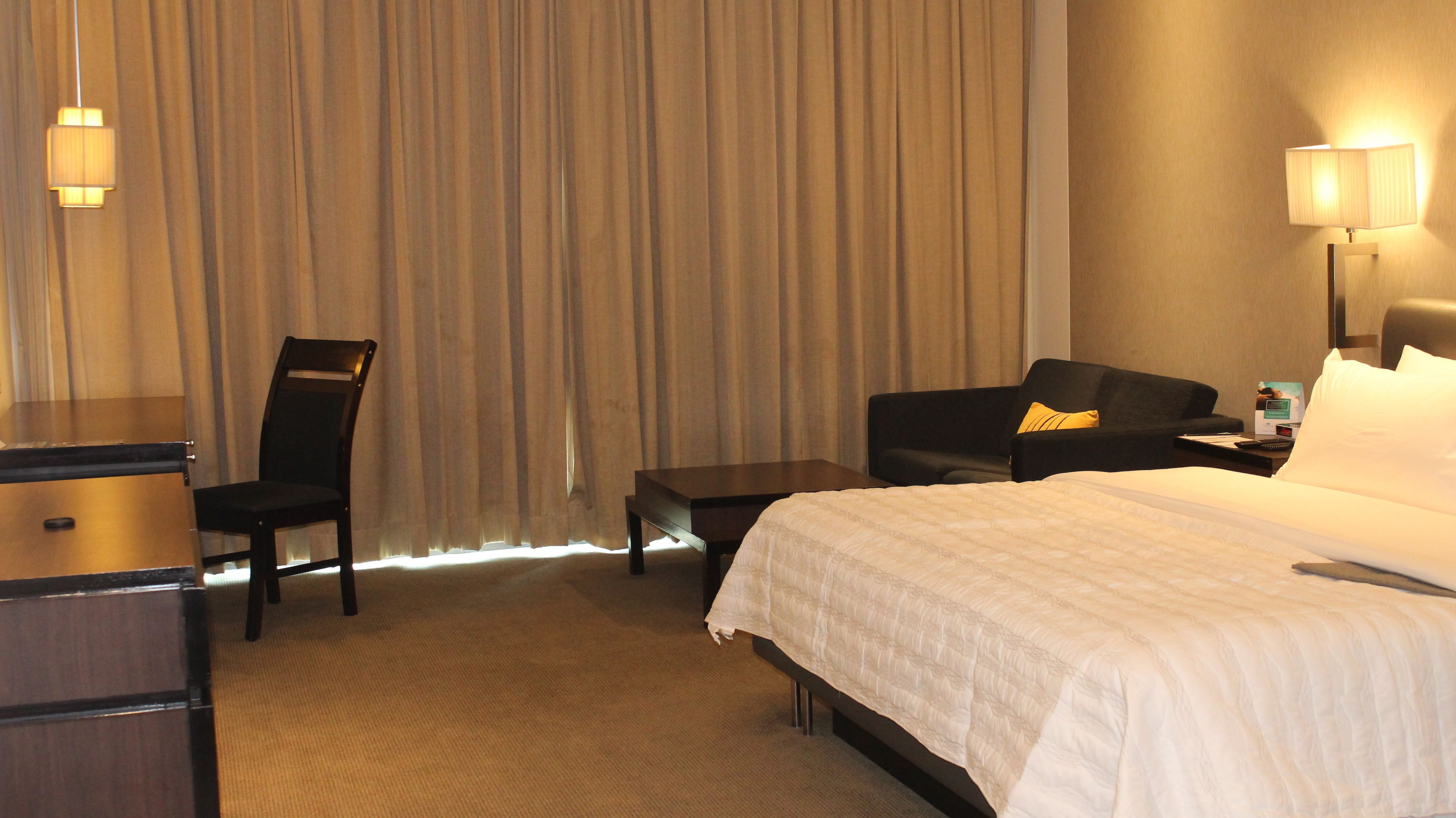 Habitación de hotel con cama, escritorio, silla, sofá y mesita de noche con lámpara.