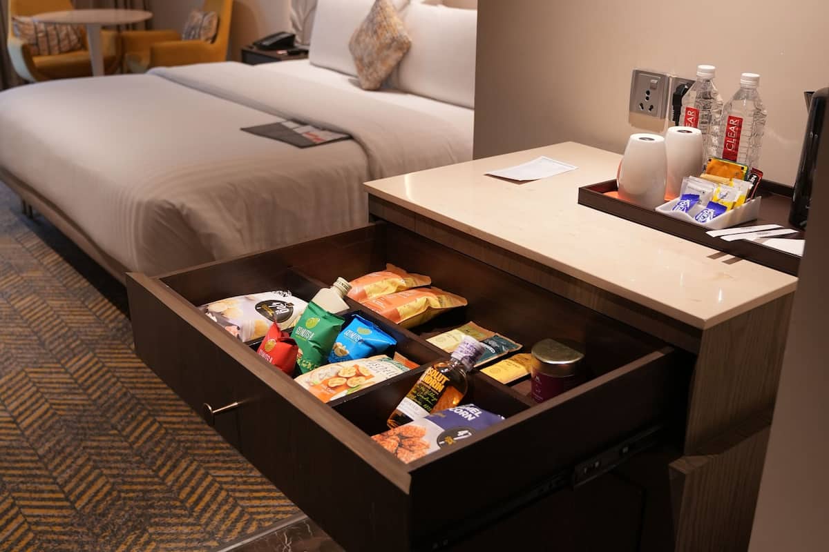 A hotel room with a bed, a desk with a drawer, a chair, and a carpeted floor.