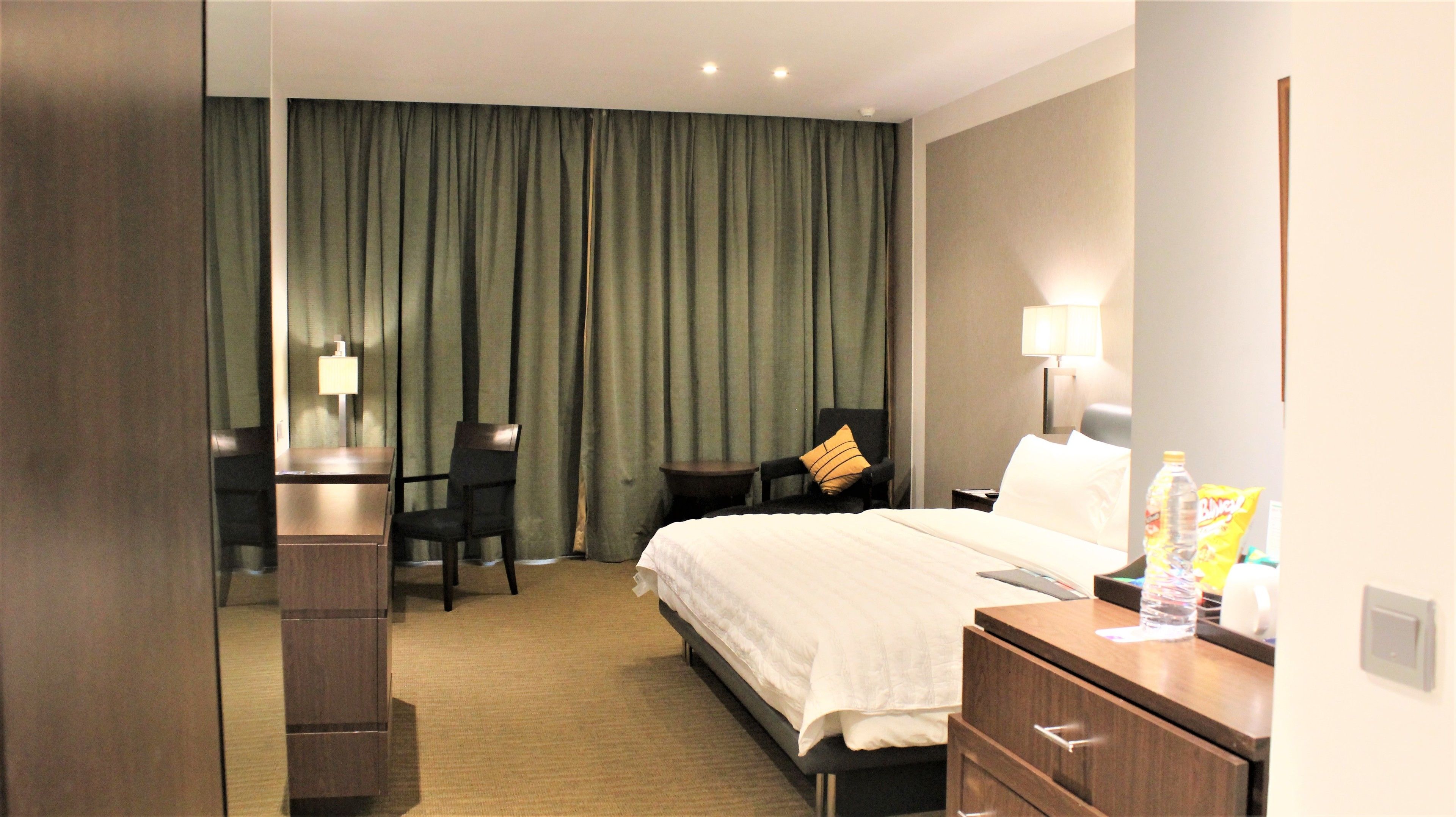 A hotel room with a bed, a desk, a chair, a nightstand, and a lamp.