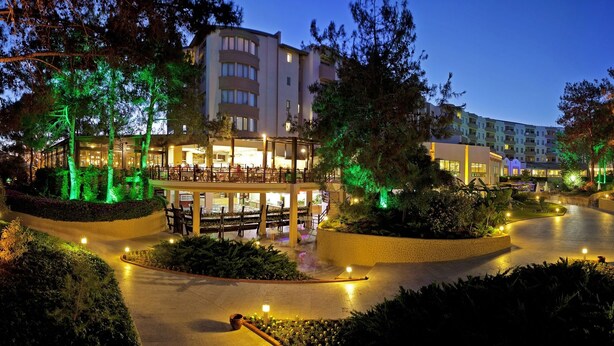 A well-lit outdoor area with a curved pathway, surrounded by trees and buildings. - Sueno Hotels Beach Side (Manavgat)