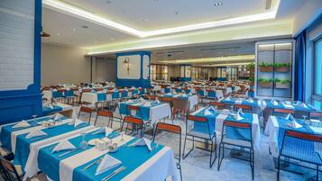 A large banquet hall with rows of tables set for dining, featuring blue tablecloths and white napkins.