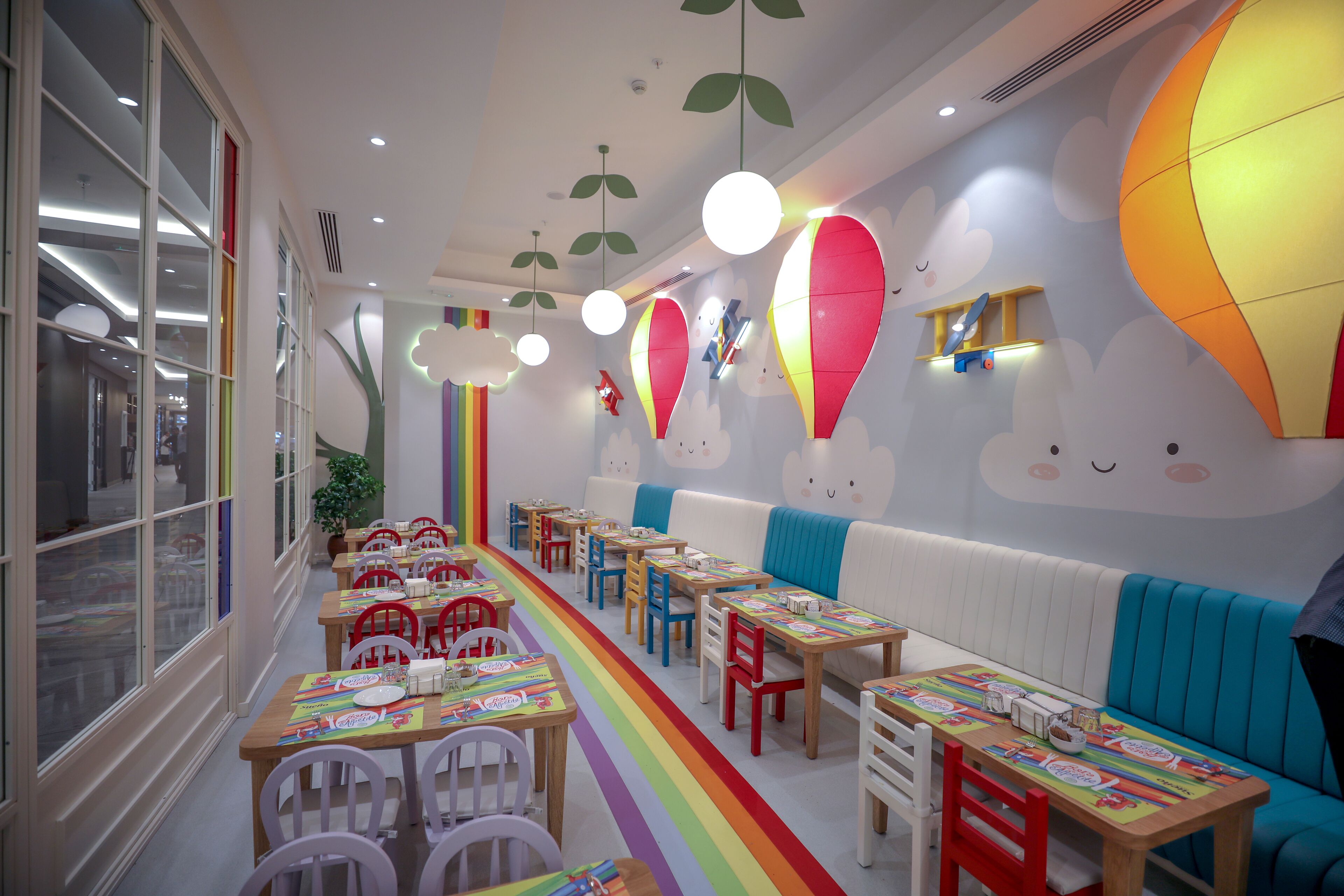 Un área de comedor infantil con mesas, sillas y un suelo de colores del arcoíris.