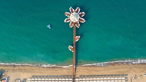 An aerial view of a beach resort with a central pier, rows of beach umbrellas, and a pool area. - Sueno Hotels Beach Side (Manavgat)