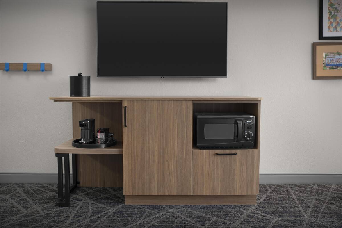 A modern kitchenette with a microwave, coffee maker, and a flat-screen TV mounted on the wall.