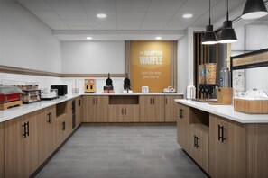 A modern kitchen with wooden cabinets, a coffee station, and a waffle station. - Hampton Inn & Suites Laurel, MS (Laurel)