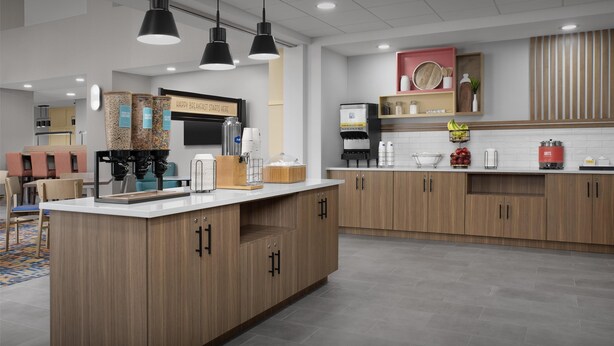 Una cocina moderna con armarios de madera, una isla central, iluminación colgante y una zona con barra desayunadora.