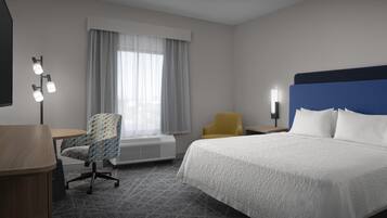 Una habitación de hotel con una cama, un escritorio, una silla y un ventanal con cortinas.