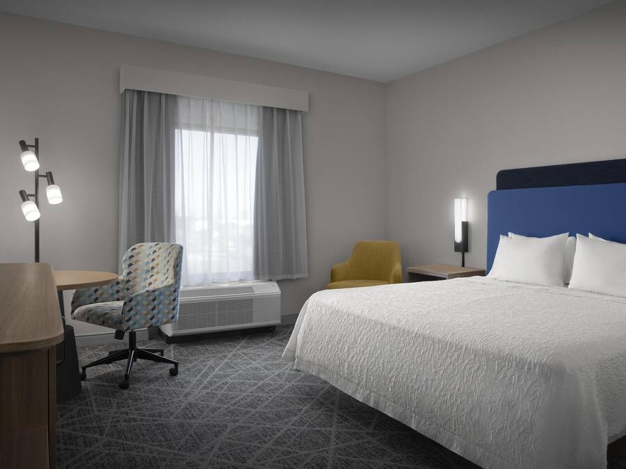 Una habitación de hotel con una cama, un escritorio, una silla y un ventanal con cortinas.
