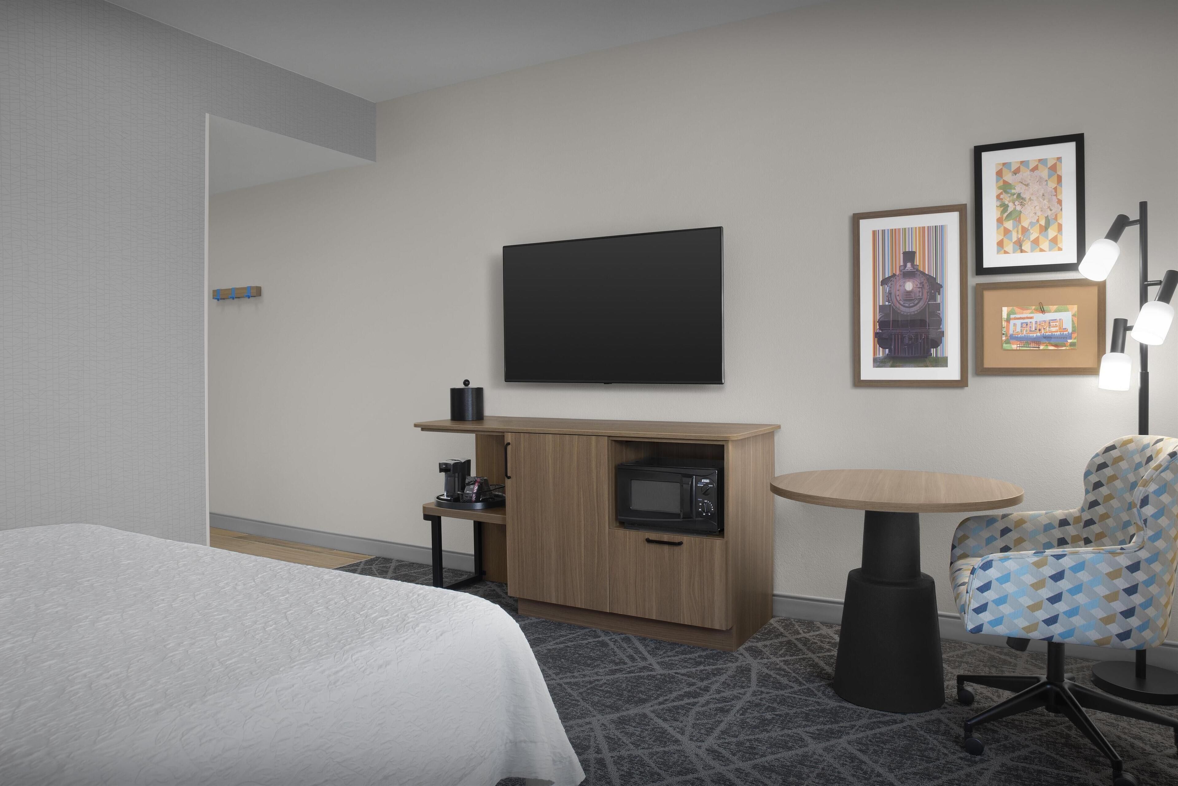 Ett hotellrum med en säng, en TV, en mikrovågsugn, ett litet bord och en stol.
