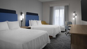 Habitación de hotel con dos camas, un escritorio, una silla y una lámpara.