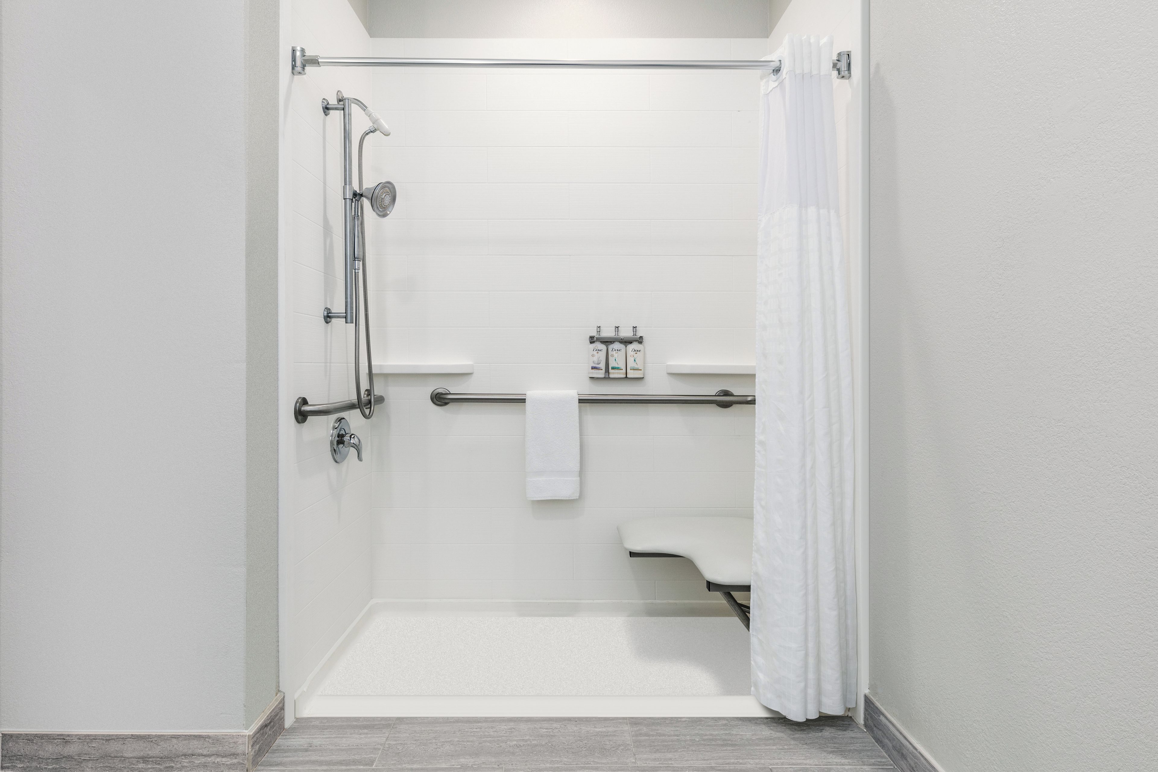 Une douche à l’italienne avec une porte en verre, une douchette à main, un flexible de douche, un robinet de douche à main, un porte-serviettes et une petite étagère pour les articles de toilette.