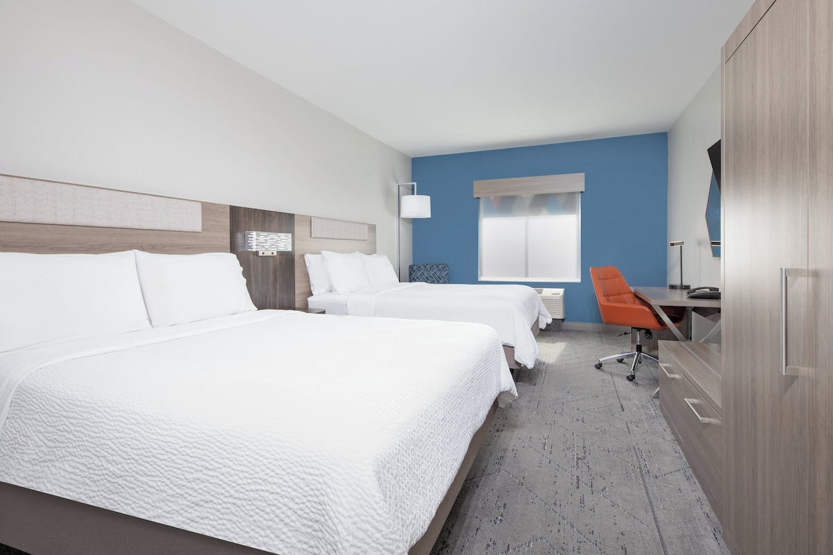 A hotel room with two beds, a desk, an orange chair, and a wardrobe.