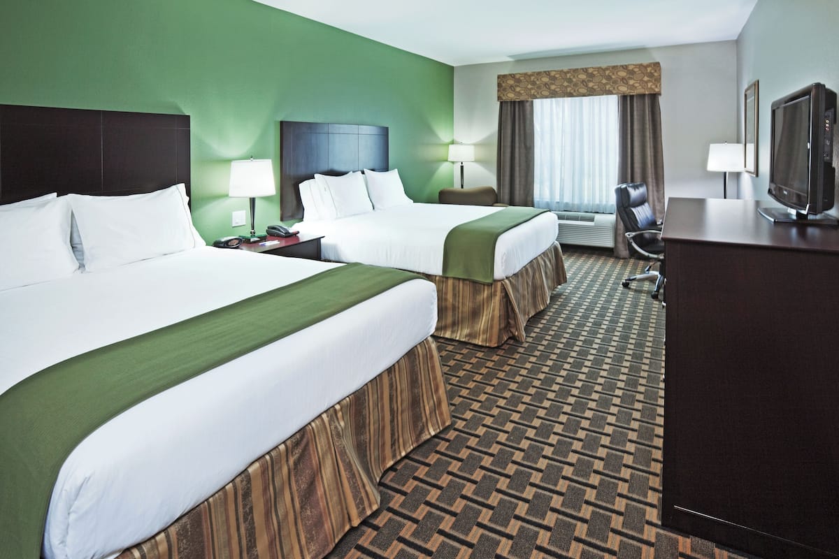 A hotel room with two beds, a desk with a television, and a window with curtains.