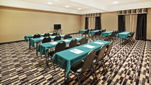 Un salón de conferencias con varias mesas y sillas, un televisor de pantalla plana y una alfombra estampada.