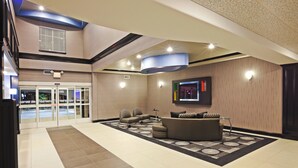 A lobby with a reception desk, seating area, and a television screen. - Holiday Inn Express Hotel & Suites JACKSONVILLE by IHG (Jacksonville)