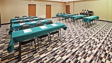 A conference room with multiple tables, chairs, and a kitchenette area.