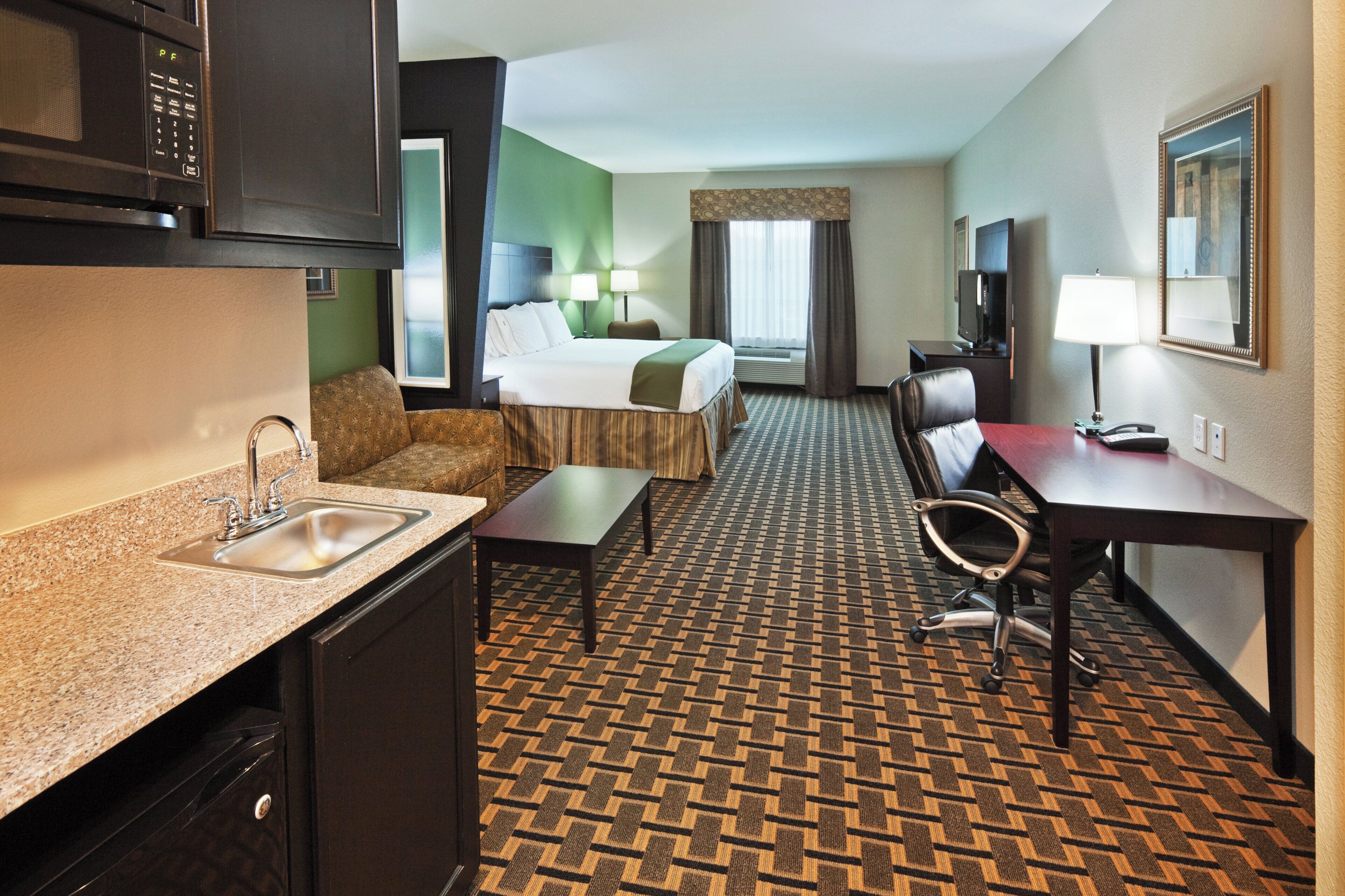 Una habitación de hotel con kitchenette, cama, escritorio, silla y televisor.