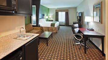 Una habitación de hotel con kitchenette, cama, escritorio, silla y televisor.