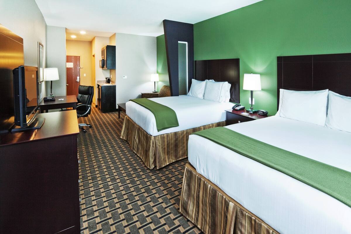 A hotel room with two beds, a desk, a chair, a TV, and a bathroom.