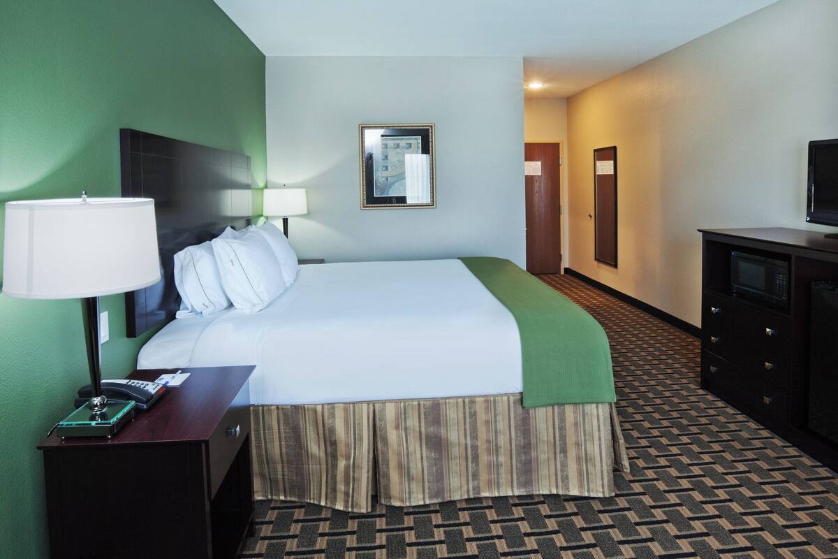 A hotel room with a bed, a desk with a lamp, a telephone, a television, and a dresser.