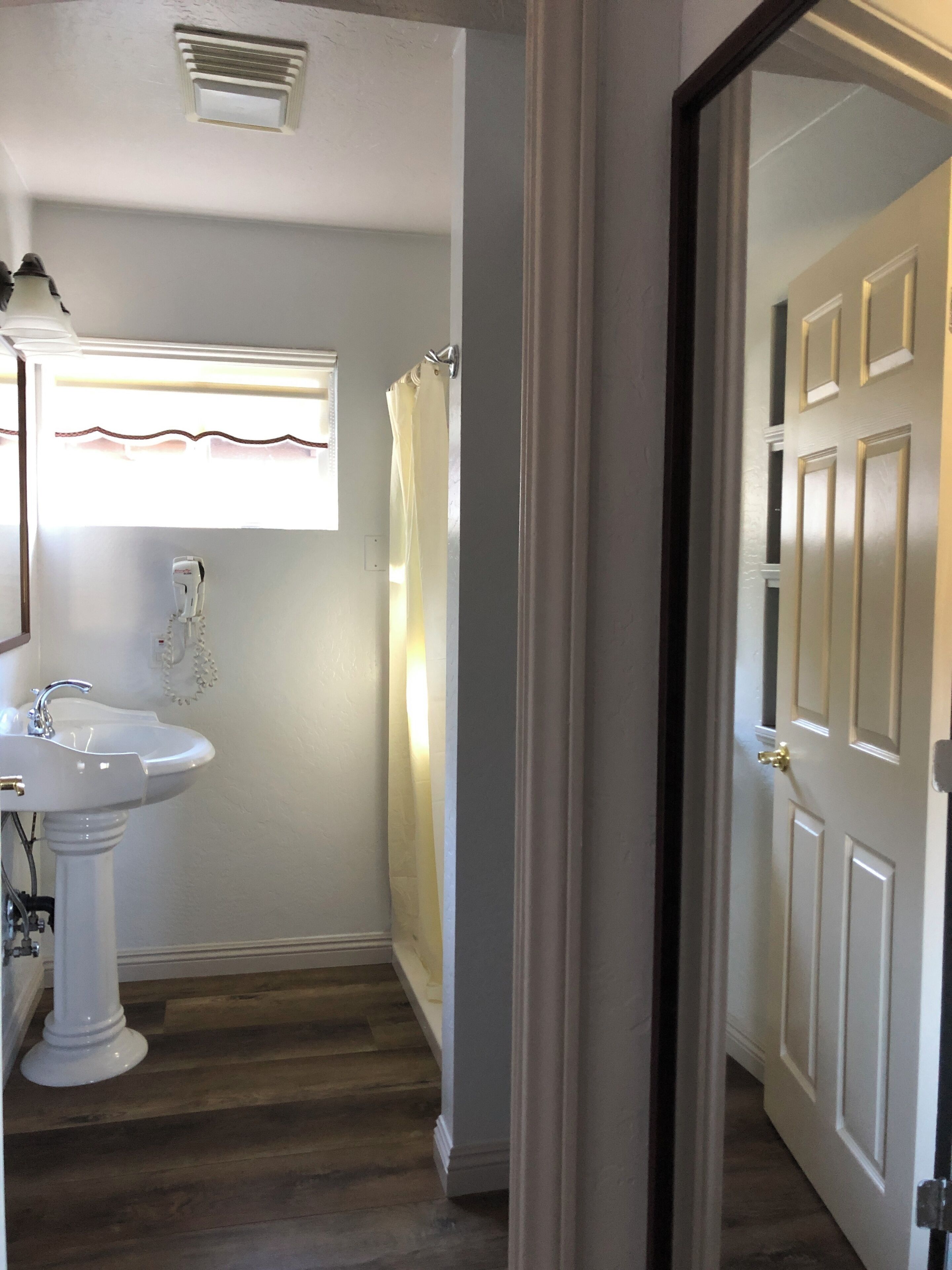 A bathroom with a white sink, a shower curtain, and a door leading to another room.