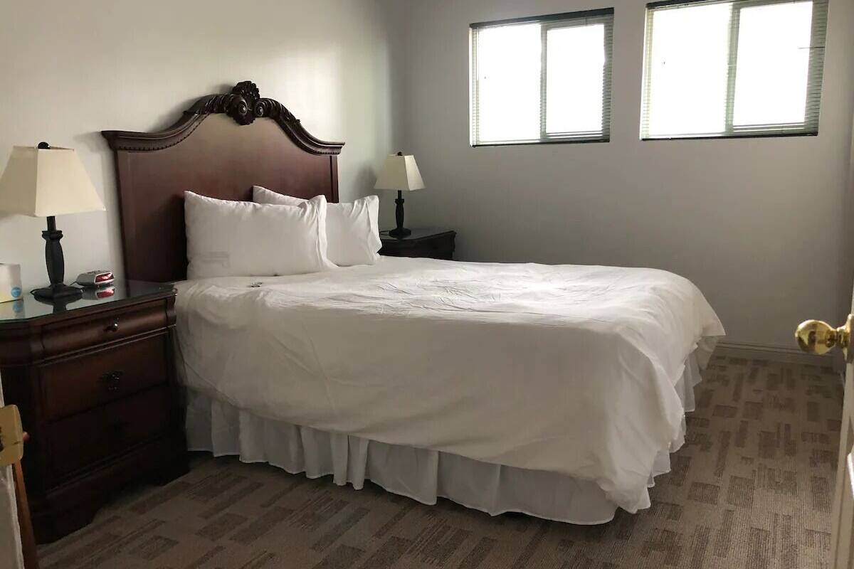A neatly made bed with white linens, a wooden headboard, and two bedside lamps.